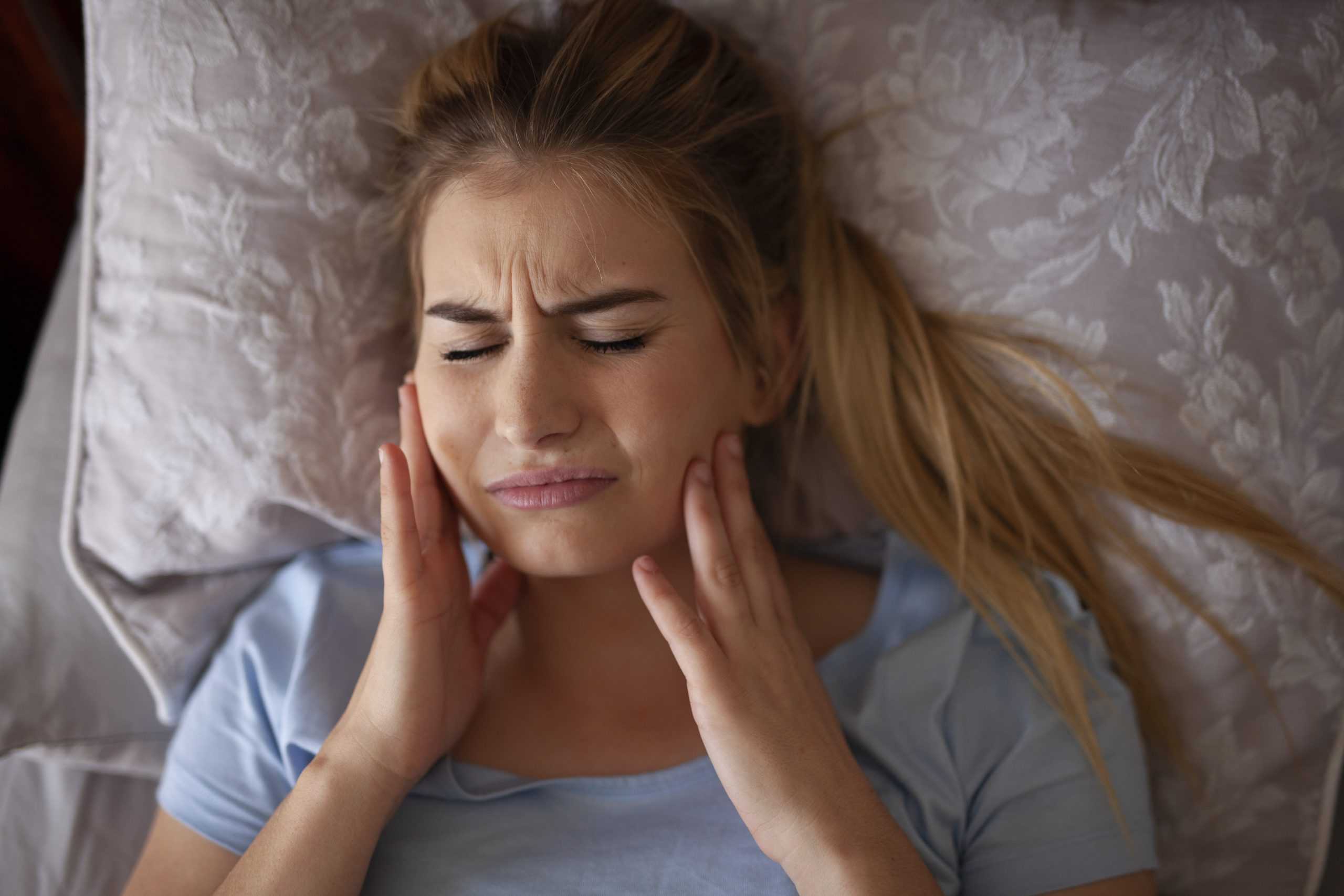 A woman lays in bed in pain from TMJ disorder.