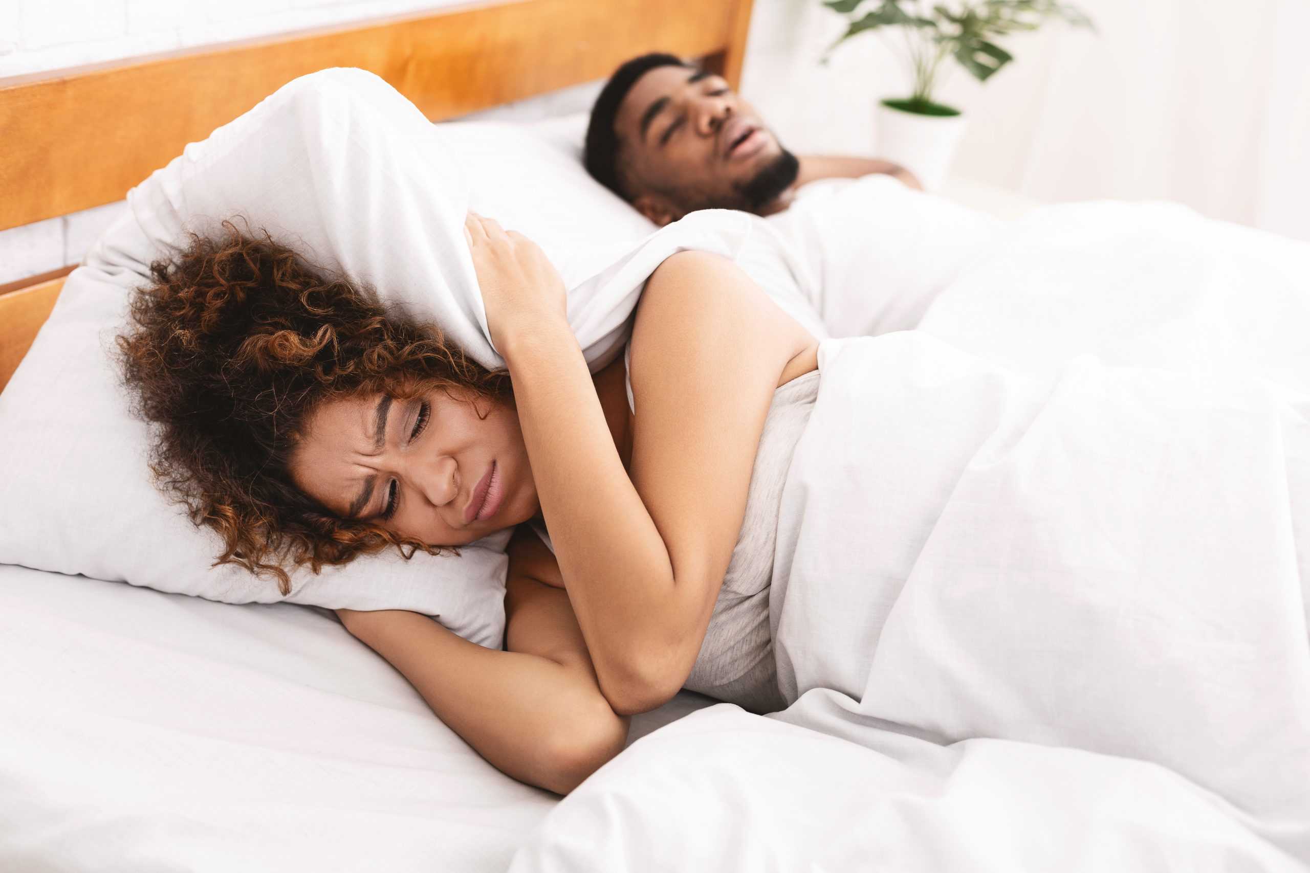 Woman covers her ears with a pillow as husband snores.