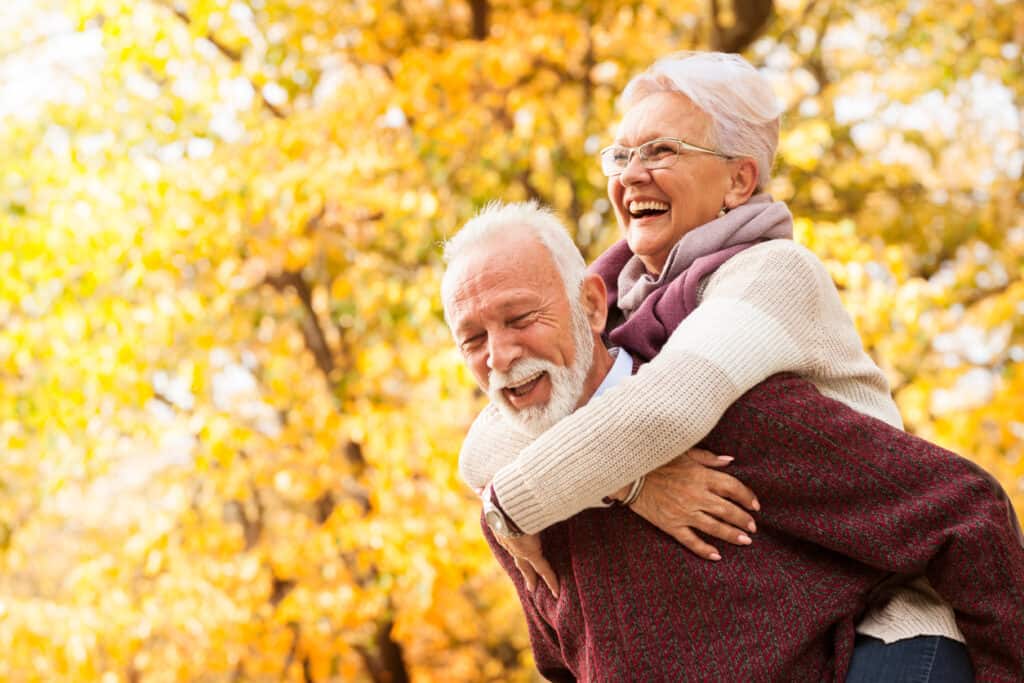 Senior man giving wife a piggy back ride with Fall leaves in the background