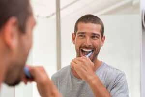 Man brushing his teeth while looking in the mirror